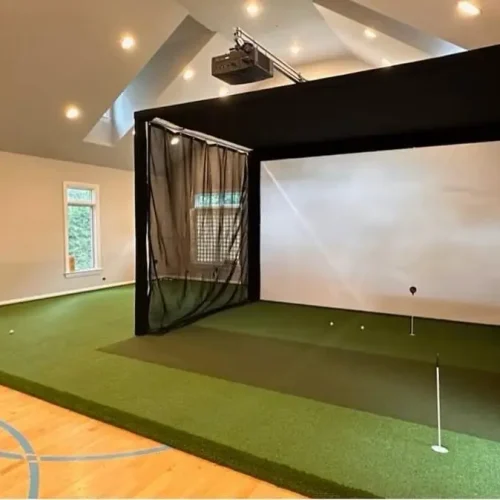 Indoor golf simulator with synthetic putting green, practice holes, and surrounding golf turf