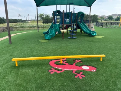 Commercial playground artificial turf with shaded play equipment and custom colorful lizard graphic