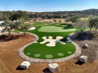 Private short-game golf complex with synthetic putting green, sand bunkers, target areas, and surrounding golf turf in Austin, Texas